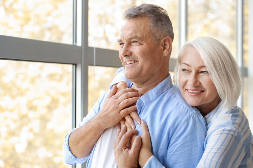 Smiling senior couple standing together by a bright window